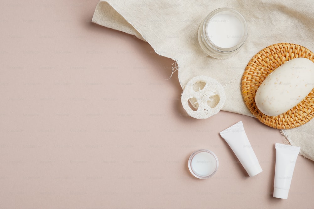 SPA natural organic cosmetics set with towel on beige background. Flat lay, top view moisturizer cream, homemade soap, cream tubes, loofah. Skin care concept.