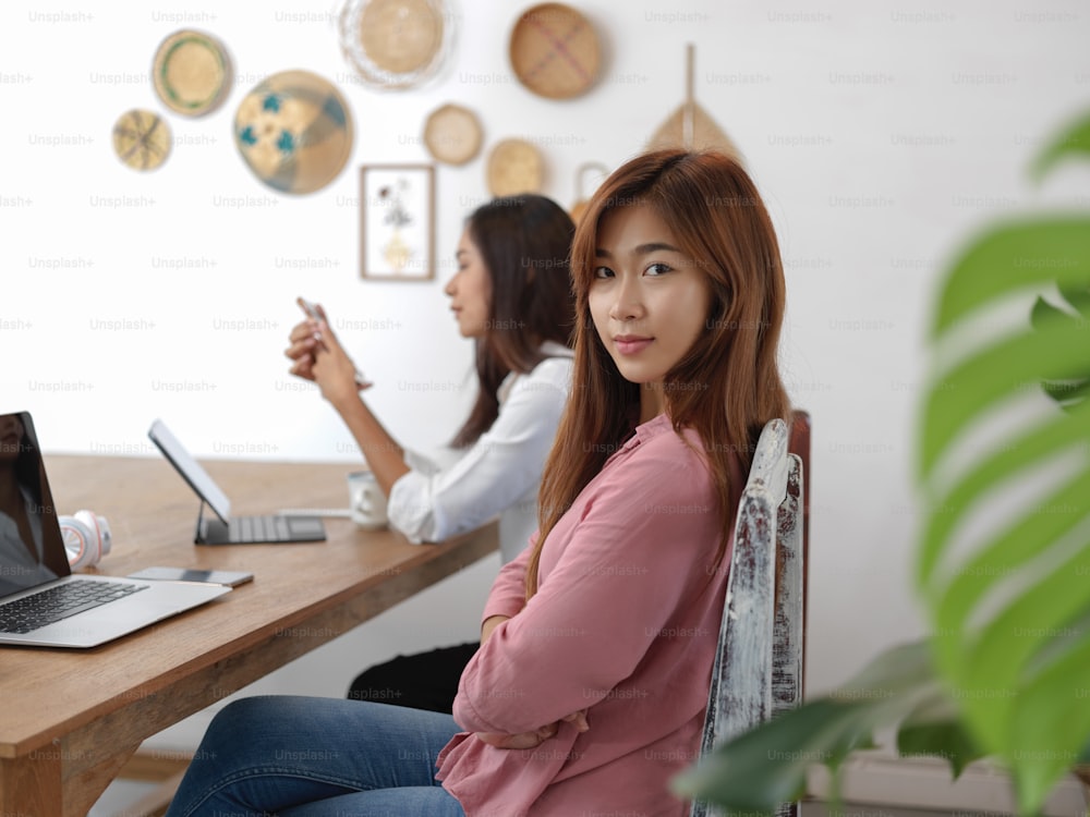 Portrait of female university student sitting on chair at table in cafe with her friend and digital devices