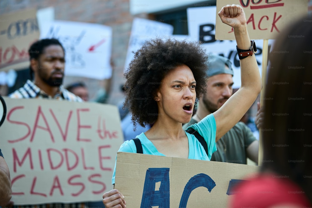 Mulher afro-americana desagradada protestando com multidão de pessoas e gritando com o punho erguido.