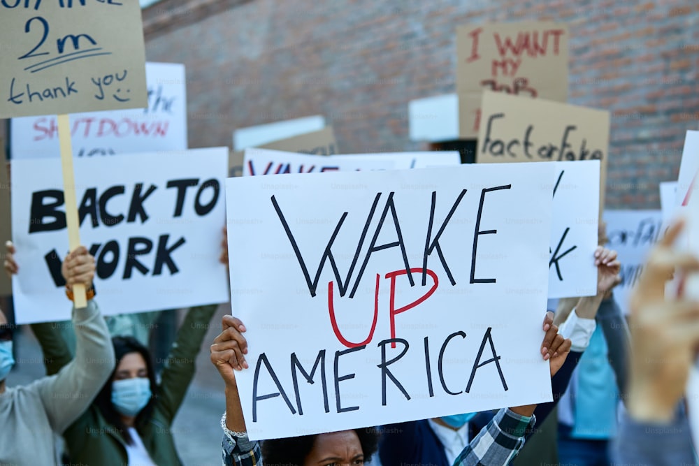 Primo piano di una persona che tiene un cartello con l'iscrizione americana sveglia su una protesta durante l'epidemia di coronavirus.