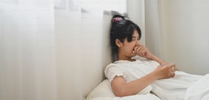 Une femme malade tient un verre d’eau et consomme une pilule alors qu’elle est allongée sur le lit de la chambre.