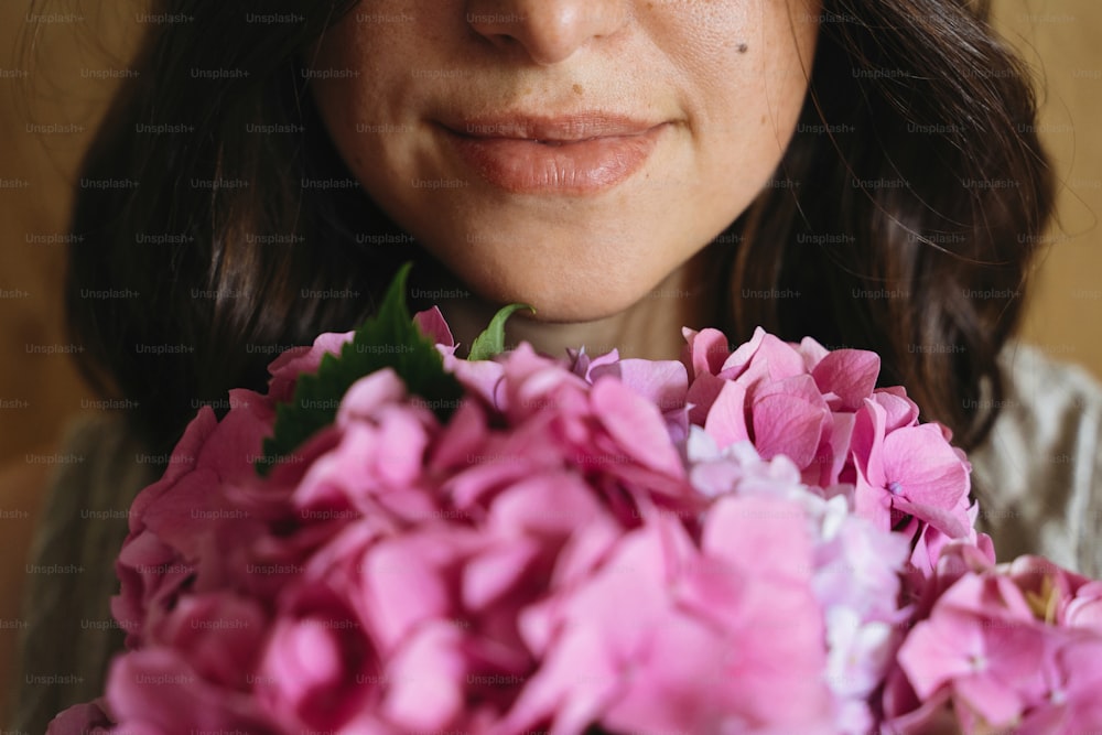 Mulher nova cheirando buquê de hortênsia bonita no fundo da madeira rústica. Menina segurando flores de hortênsia rosa e roxa, vista cortada. Aroma bonito