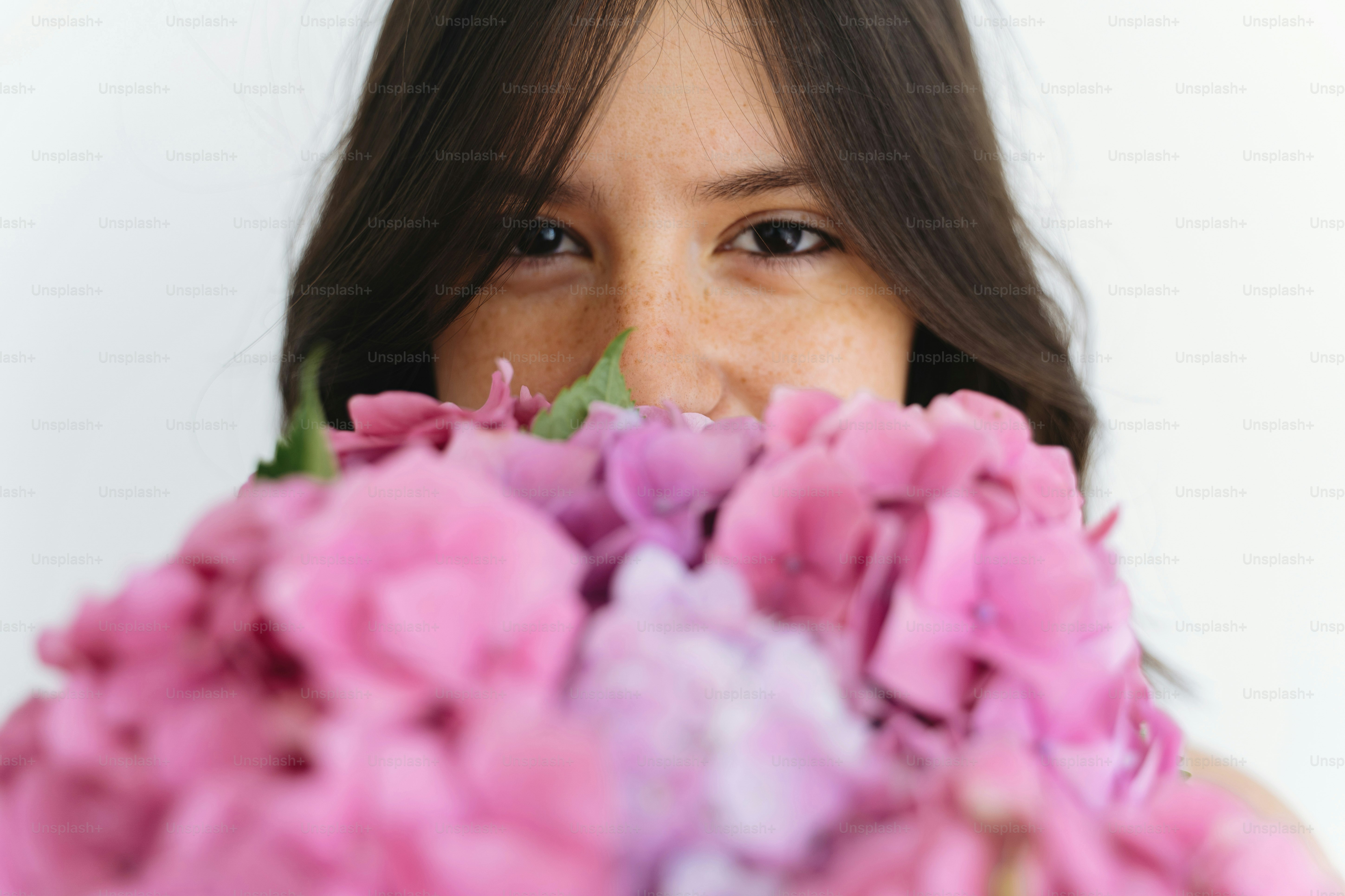 Young woman smelling beautiful hydrangea bouquet on background of white wall. Stylish girl holding pink and purple hydrangea flowers. Happy mothers day or womens day.