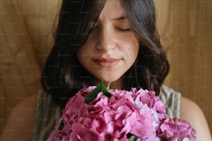 Young woman smelling beautiful hydrangea bouquet on background of  rustic wood. Stylish girl holding pink and purple hydrangea flowers. Happy mothers day or womens day.