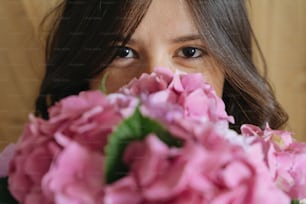 Junge Frau duftet nach schönem Hortensienstrauß auf dem Hintergrund aus rustikalem Holz. Stilvolles Mädchen mit rosa und lila Hortensienblüten. Alles Gute zum Muttertag oder Frauentag.
