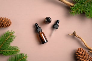Flat lay composition with bottles of conifer essential oil on beige background. Natural organic cosmetics with pine tree branches and cones