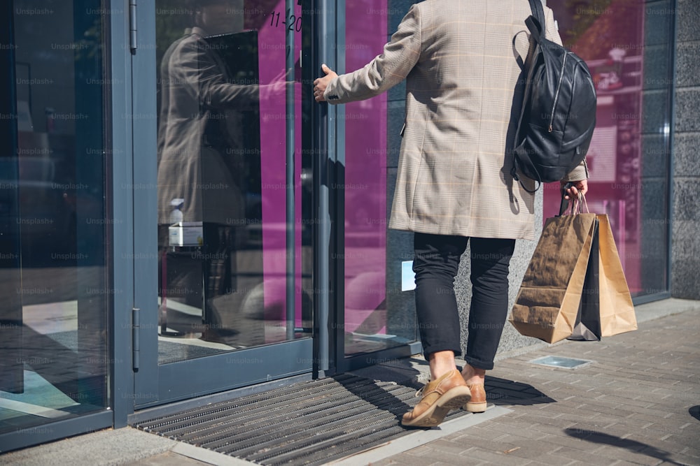 Gentleman with backpack holding shopping backs and opening boutique door