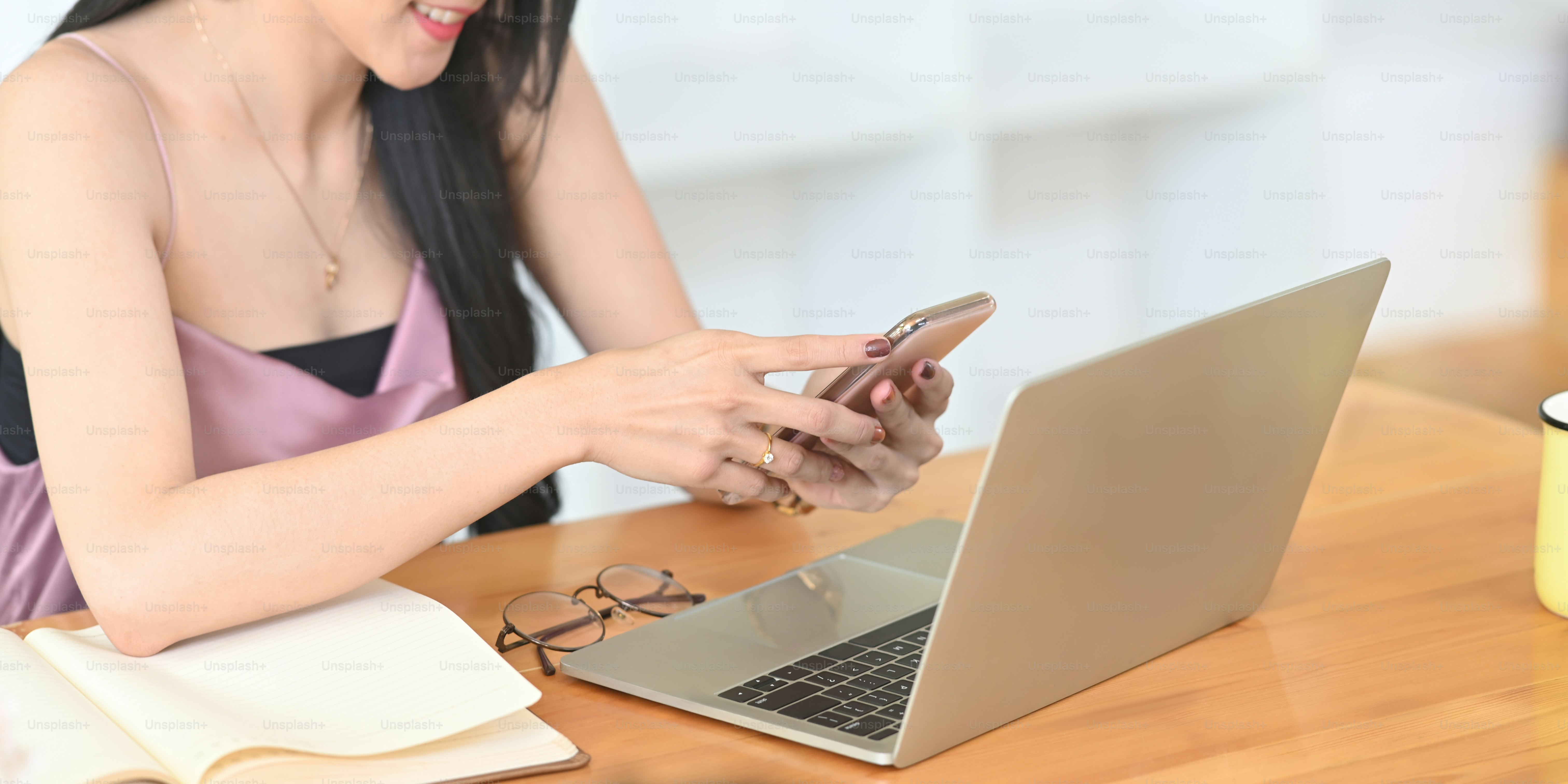 Cropped image woman is using a smartphone while sitting in front of a computer laptop at the wooden working desk.