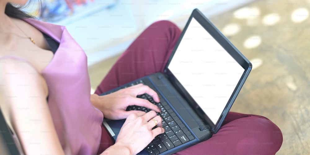 Die beschnittene Bildfrau tippt auf einem weißen Computer-Laptop mit leerem Bildschirm im Wohnzimmer.