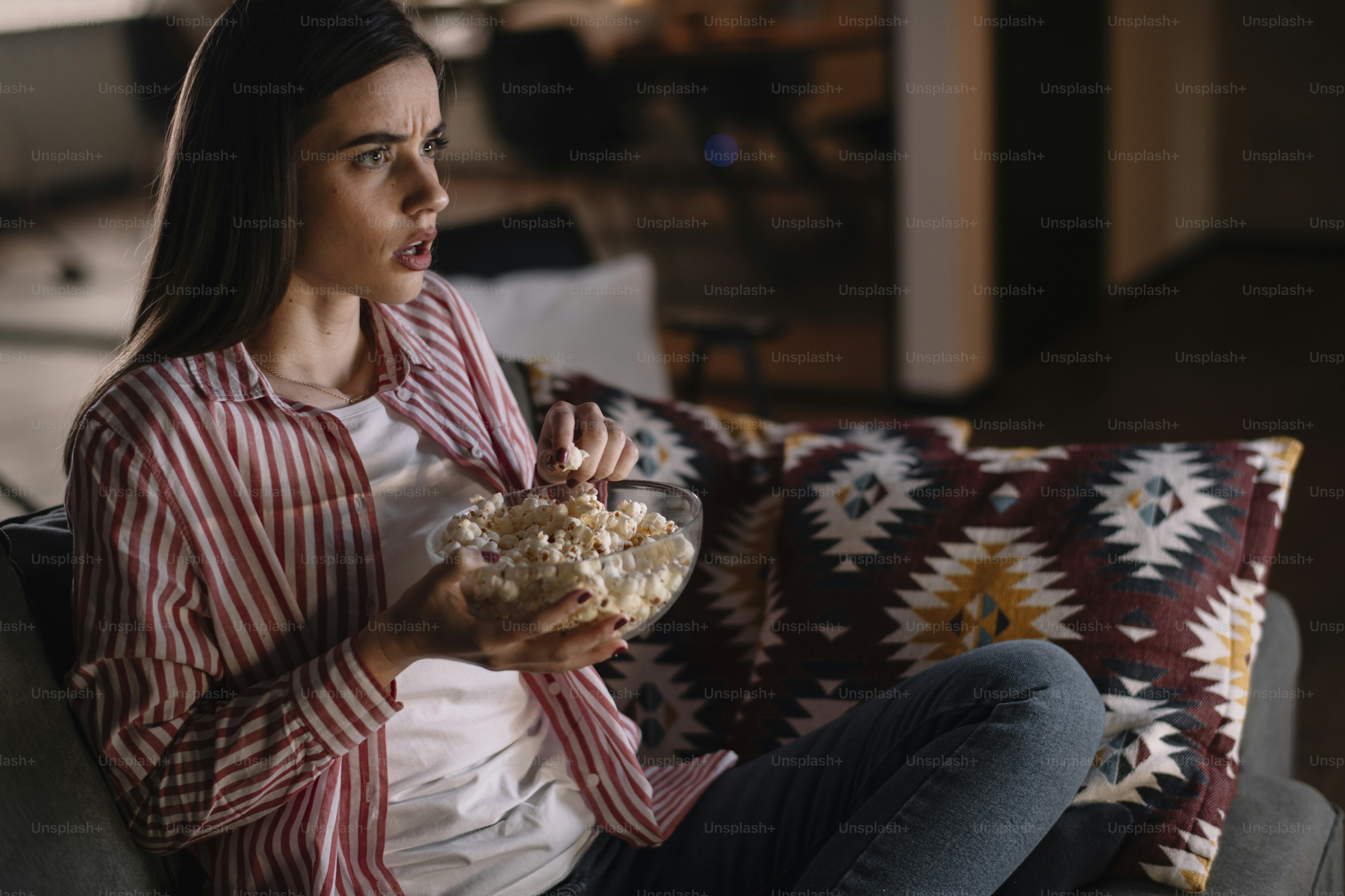 Beautiful woman watching movie in the night sitting on a couch in the living room at home