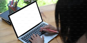 Cropped image woman is using a white blank screen computer laptop at the wooden working desk.