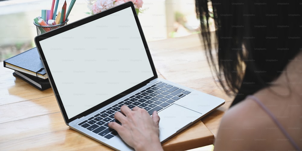 A mulher de imagem cortada está usando um laptop de computador de tela branca em branco na mesa de trabalho de madeira.