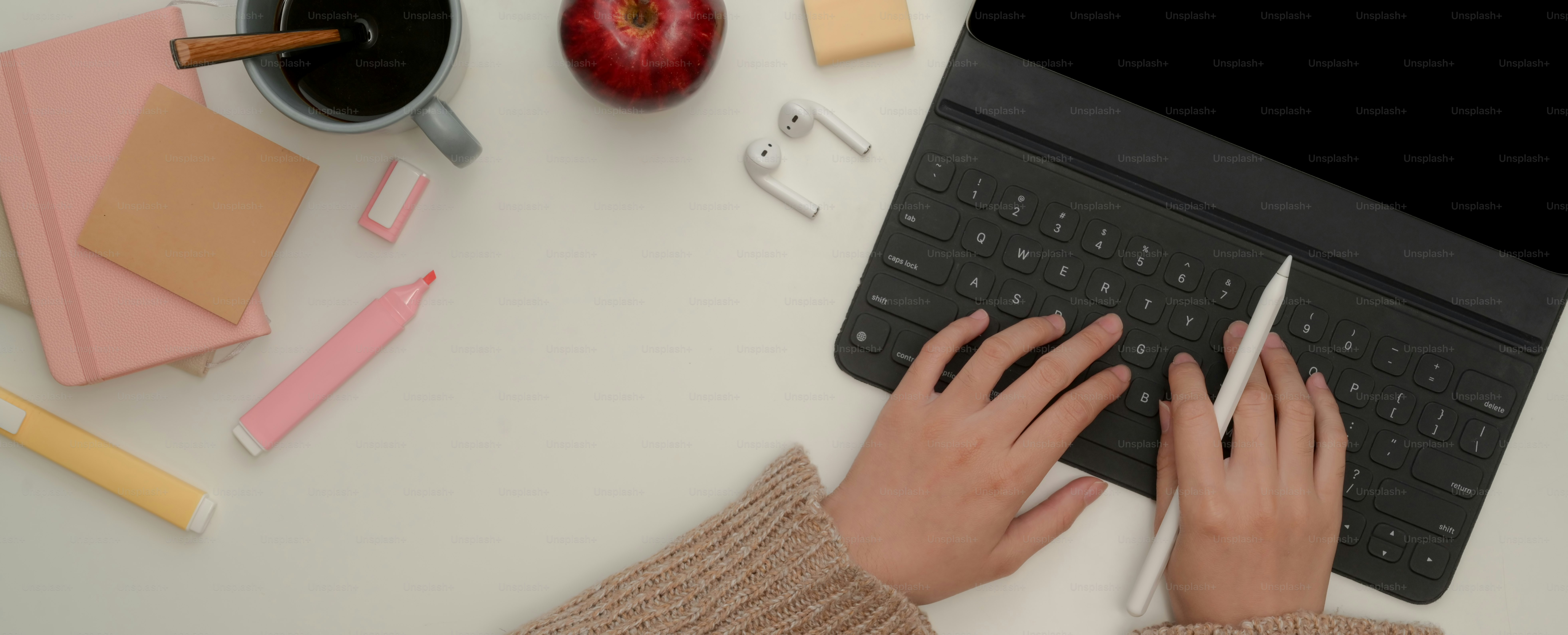 Overhead shot of female hands typing on tablet keyboard while holding stylus pen on white worktable with stationery