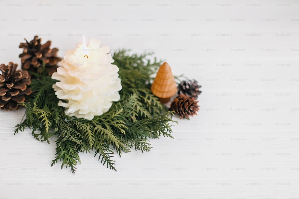 Christmas pine cone candle and tree in rustic christmas wreath on white wood. Small pine tree and modern wreath from white cedar and pine cones. Festive modern decor. Copy space