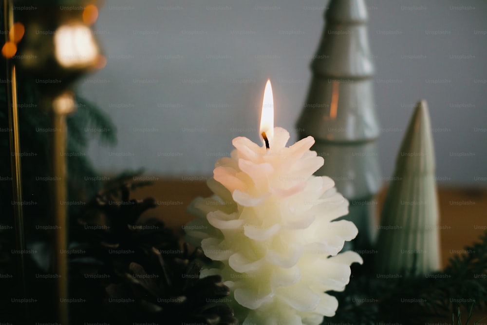 Christmas pine cone candle and trees on rustic fabric on wooden table in evening. Miniature wooden pine trees and big pine cone candle. Festive modern decor, zero waste. Happy holidays