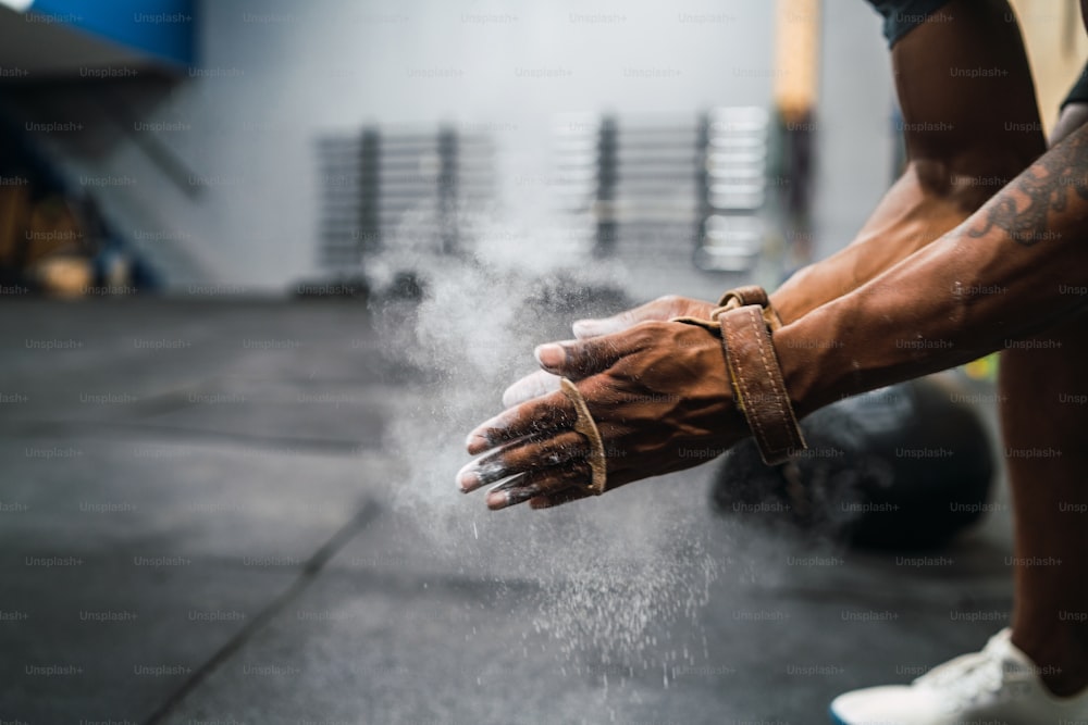 Portrait of fitness young man rubbing hands with chalk magnesium powder, preparing for workout in gym gym. Sport and healthy lifestyle concept.