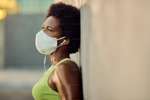 Exhausted African American sportswoman with protective face mask taking a break after exercising and leaning on a wall. Copy space.