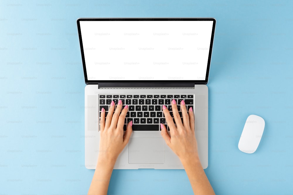 Foto aérea das mãos da mulher usando laptop com tela em branco no fundo azul. Conceito moderno de espaço de trabalho. Flat lay