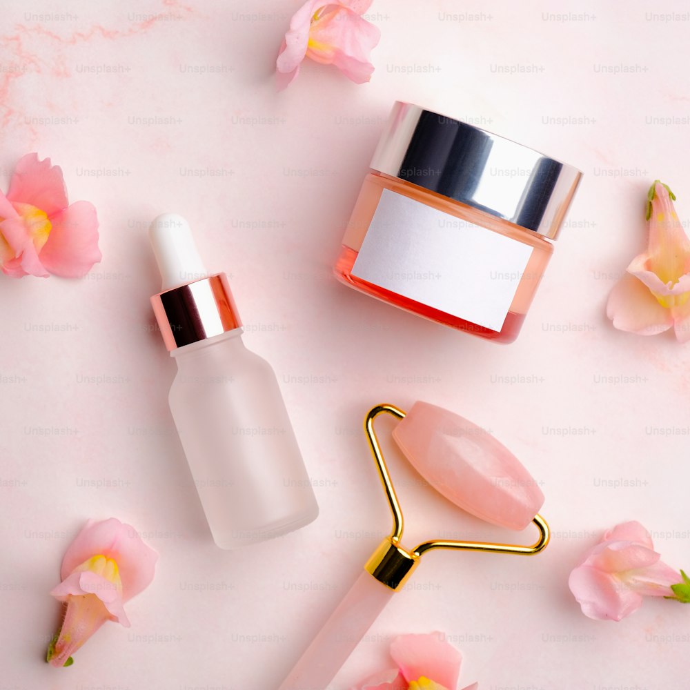 Rodillo de masaje facial, loción sérum y crema facial sobre fondo rosa. Set de productos de belleza para el cuidado de la piel.