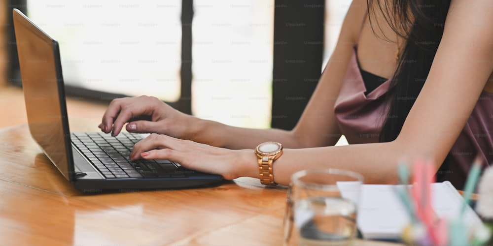 A mulher da imagem cortada está usando o laptop do computador na mesa de trabalho de madeira.