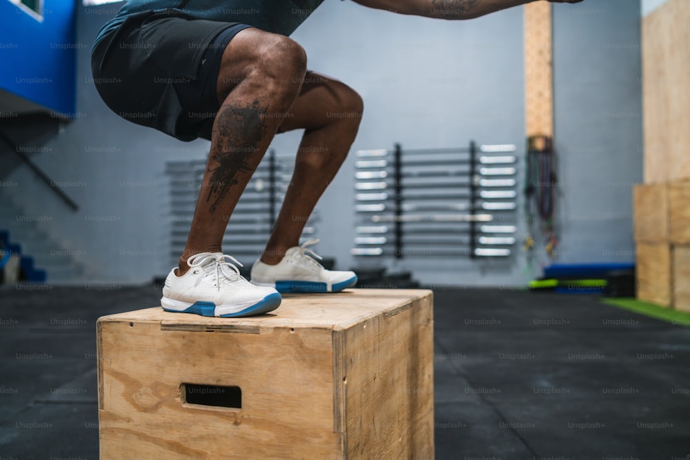 Ritratto di un uomo atletico che fa esercizio di salto in scatola. concetto di palestra, sport e stile di vita sano.