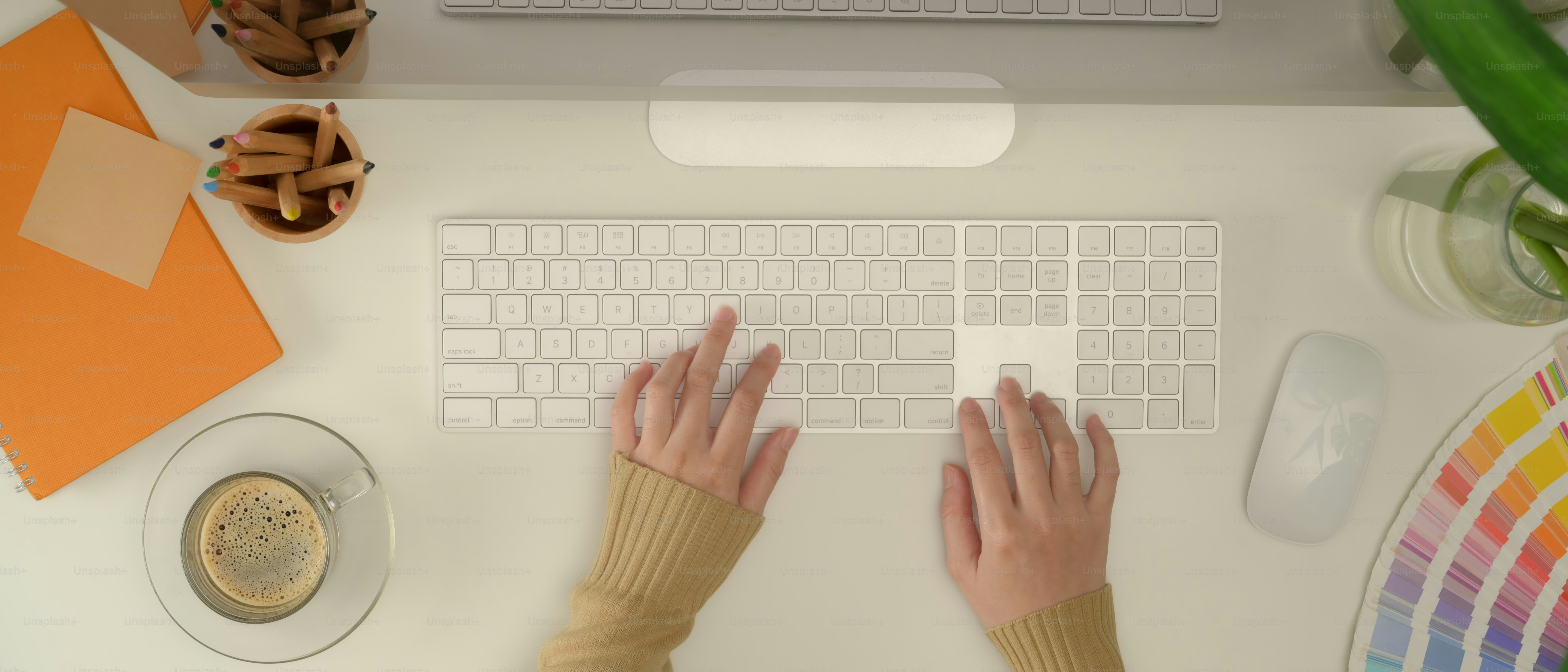 Top view of female designer typing on computer keyboard on office desk with supplies, coffee cup and decoration