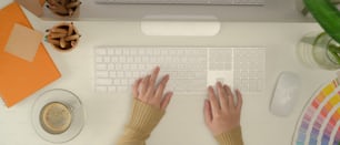 Vue de dessus d’une femme designer tapant sur le clavier d’ordinateur sur le bureau avec des fournitures, une tasse à café et une décoration