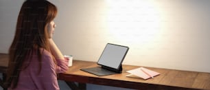 Close up view of female college student sitting at wooden counter bar and looking informations on mock-up digital tablet