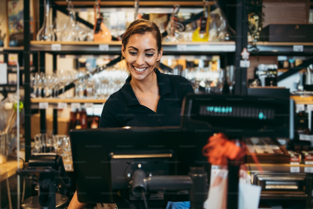 Beautiful and positive female cashier working on cash register in a modern supermarket or grocery store.