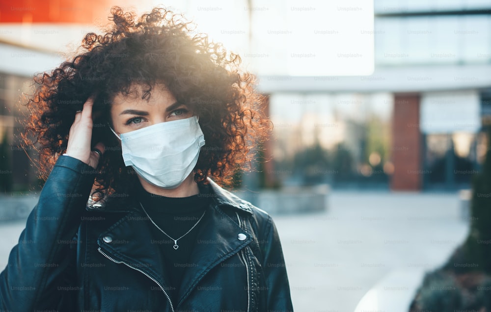 Young caucasian woman with curly hair and black leather jacket is wearing protective mask