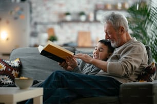 Grandfather and grandson reading a book. Grandpa and grandson enjoying at home.