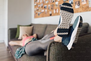 woman resting relaxed on the couch after working out in the living room dressed in sportswear. Focus on sport shoes.