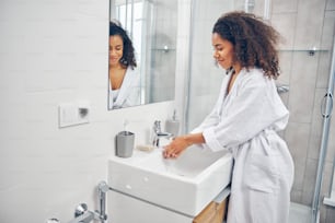 Pleased attractive young African American woman holding her cupped palms under the running tap water