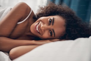 Close up portrait of a merry pretty lady with a happy smile lying on one side in bed