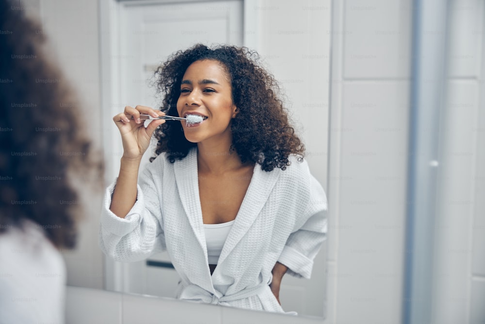 Fröhliche junge Frau mit einer Zahnbürste in der Hand betrachtet sich im Spiegel