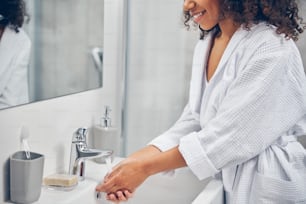 Cropped photo of a smiling pleased dark-haired woman in a bathrobe performing a handwashing procedure