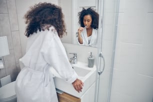 Sleepy lady with a toothbrush in her hand leaning on the sink in the bathroom