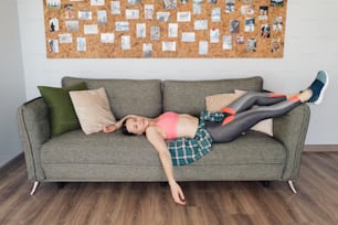 Young woman resting relaxed on the couch after working out in the living room dressed in sportswear