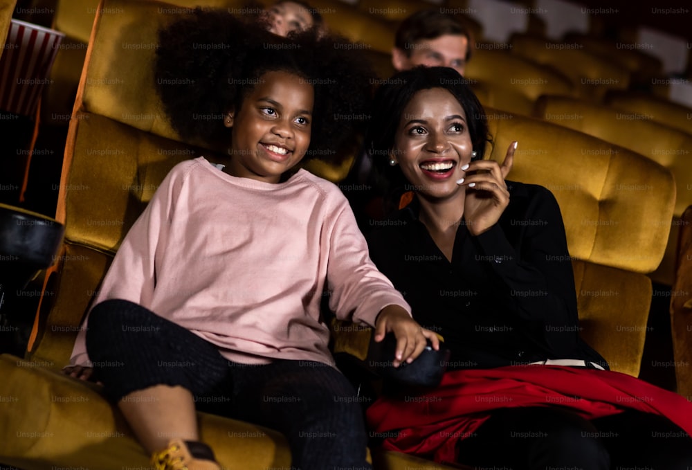 女性は映画館で娘と一緒に映画を見て笑顔で笑うのを楽しんでいます