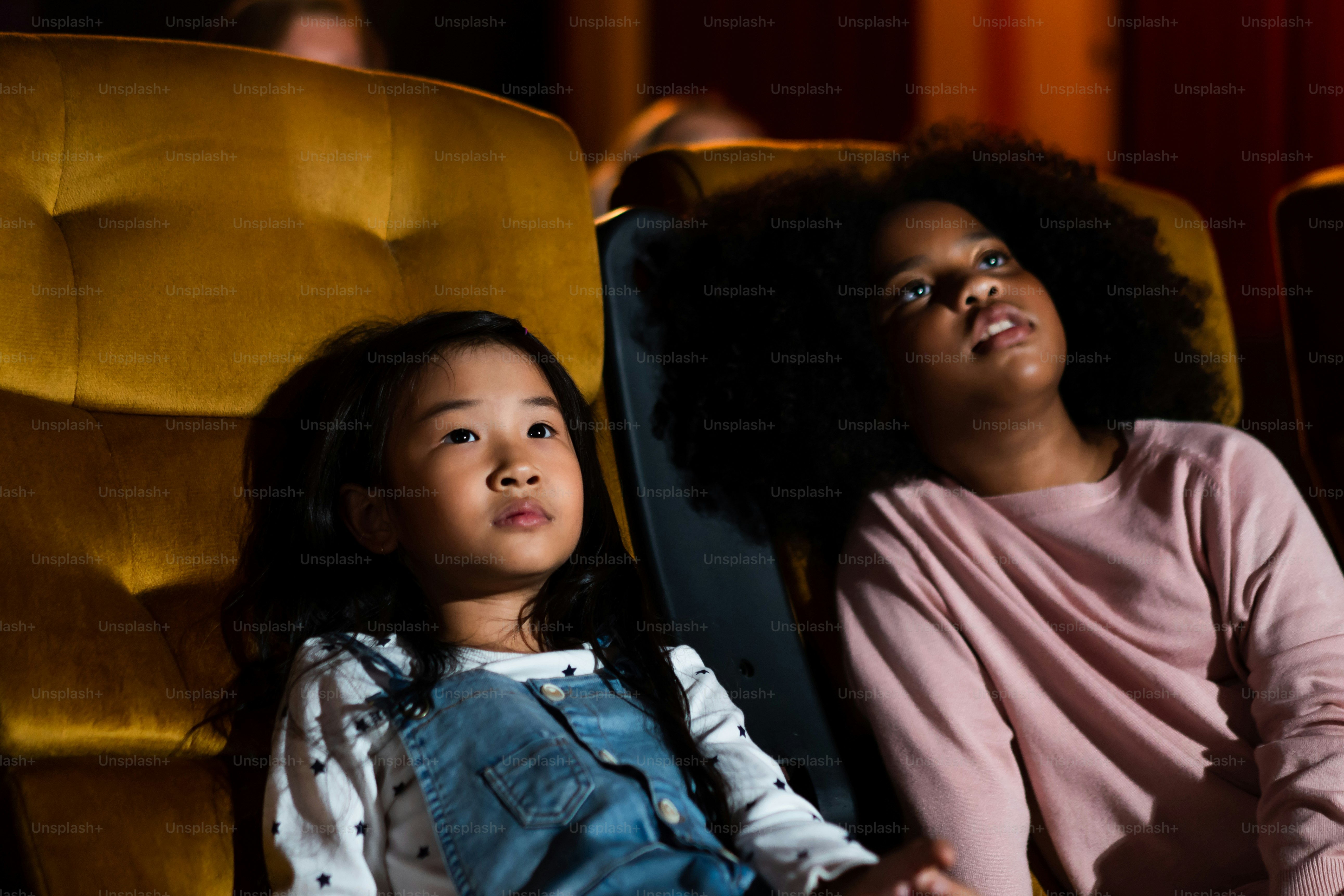 Two children african and asian having fun and enjoy watching movie in cinema
