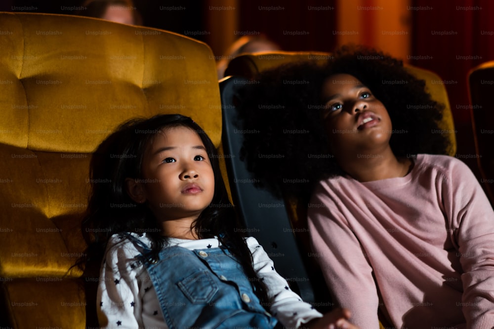 Two children african and asian having fun and enjoy watching movie in cinema