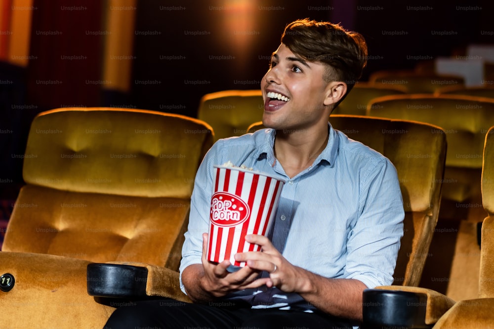 A young man smiling enjoying with his popcorn while watching a movie in theater cinema