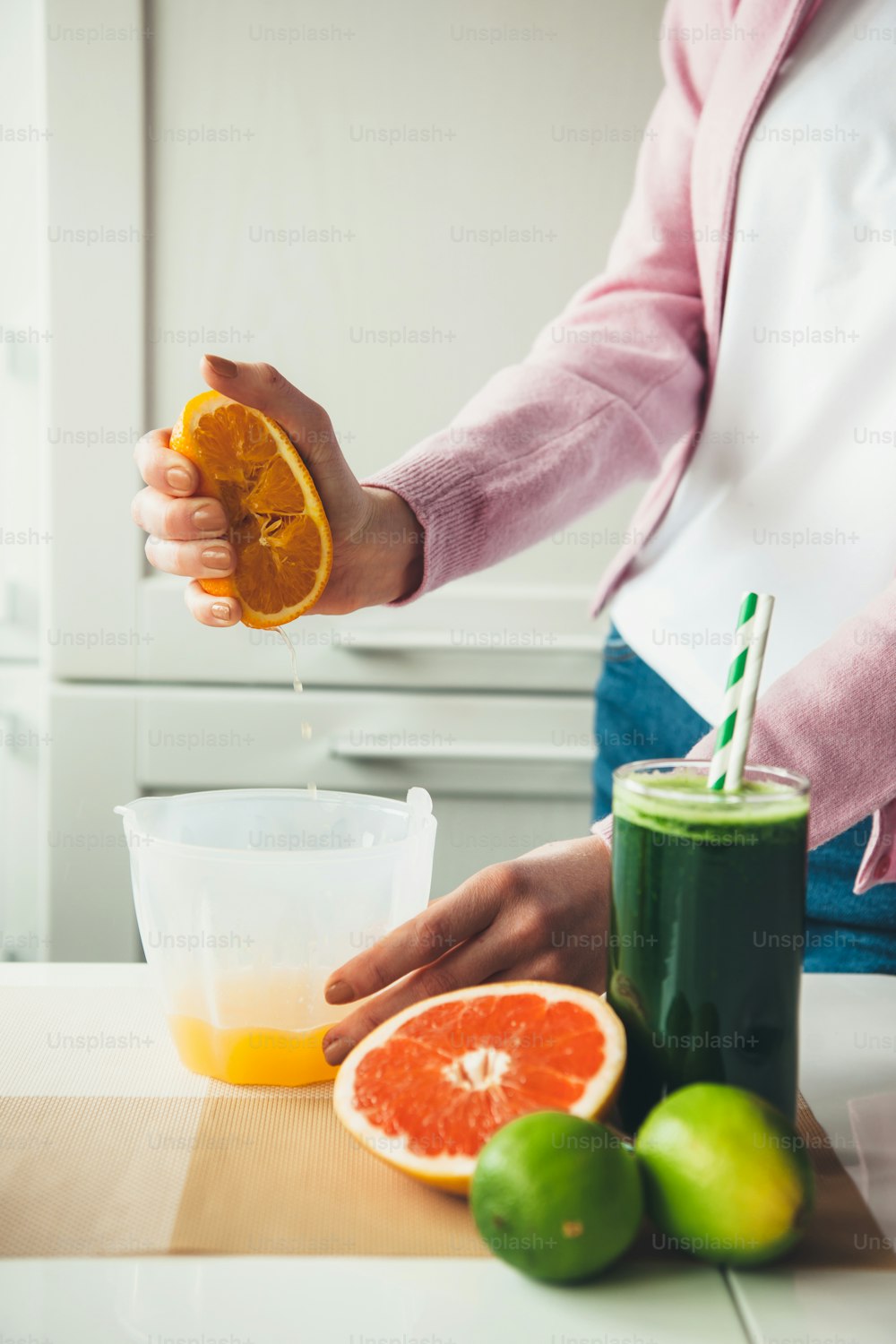 Mulher caucasiana espremendo suco de uma laranja posando perto de um copo de bebida natural