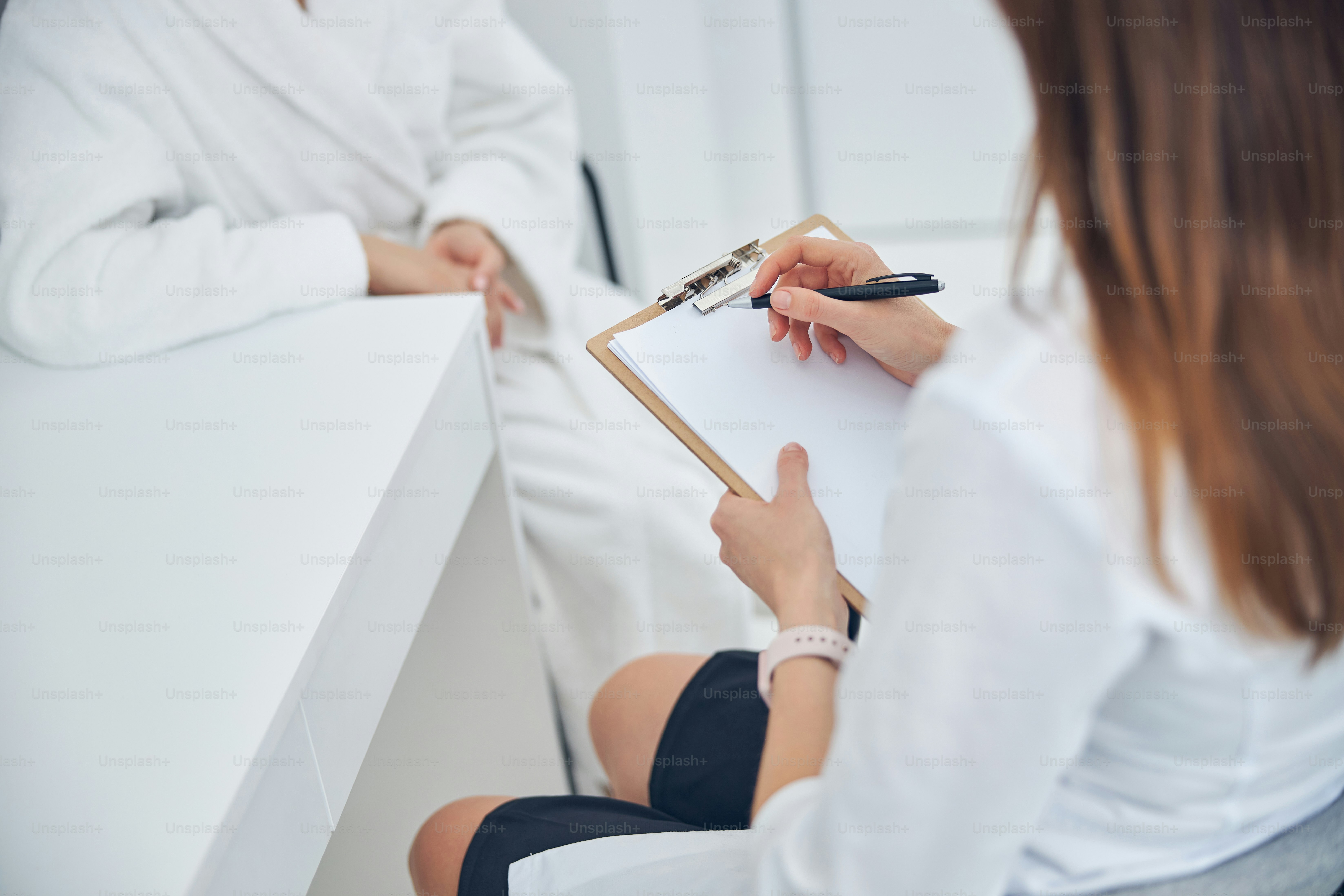 Back view portrait of doctor writing medical records on a blank sheet and holding a clipboard while sitting at the desk