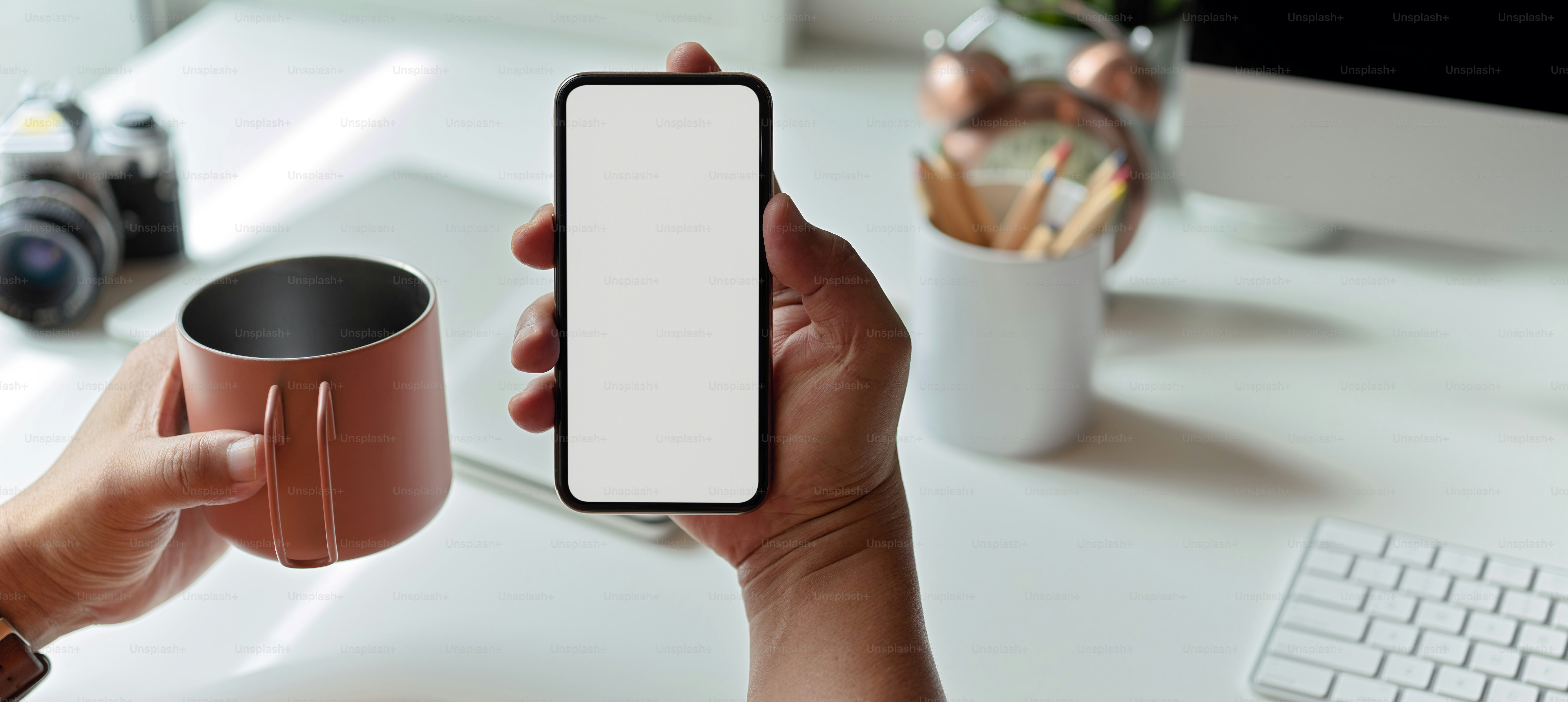 Vista de cerca de un hombre que usa un teléfono inteligente simulado y una taza de café mientras está sentado en el espacio de trabajo