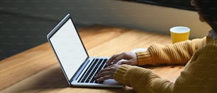 Uma mulher está digitando em um laptop de computador de tela branca em branco que coloca em uma mesa de trabalho de madeira.