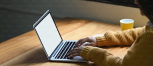 A woman is typing on a white blank screen computer laptop that putting on a wooden working desk.