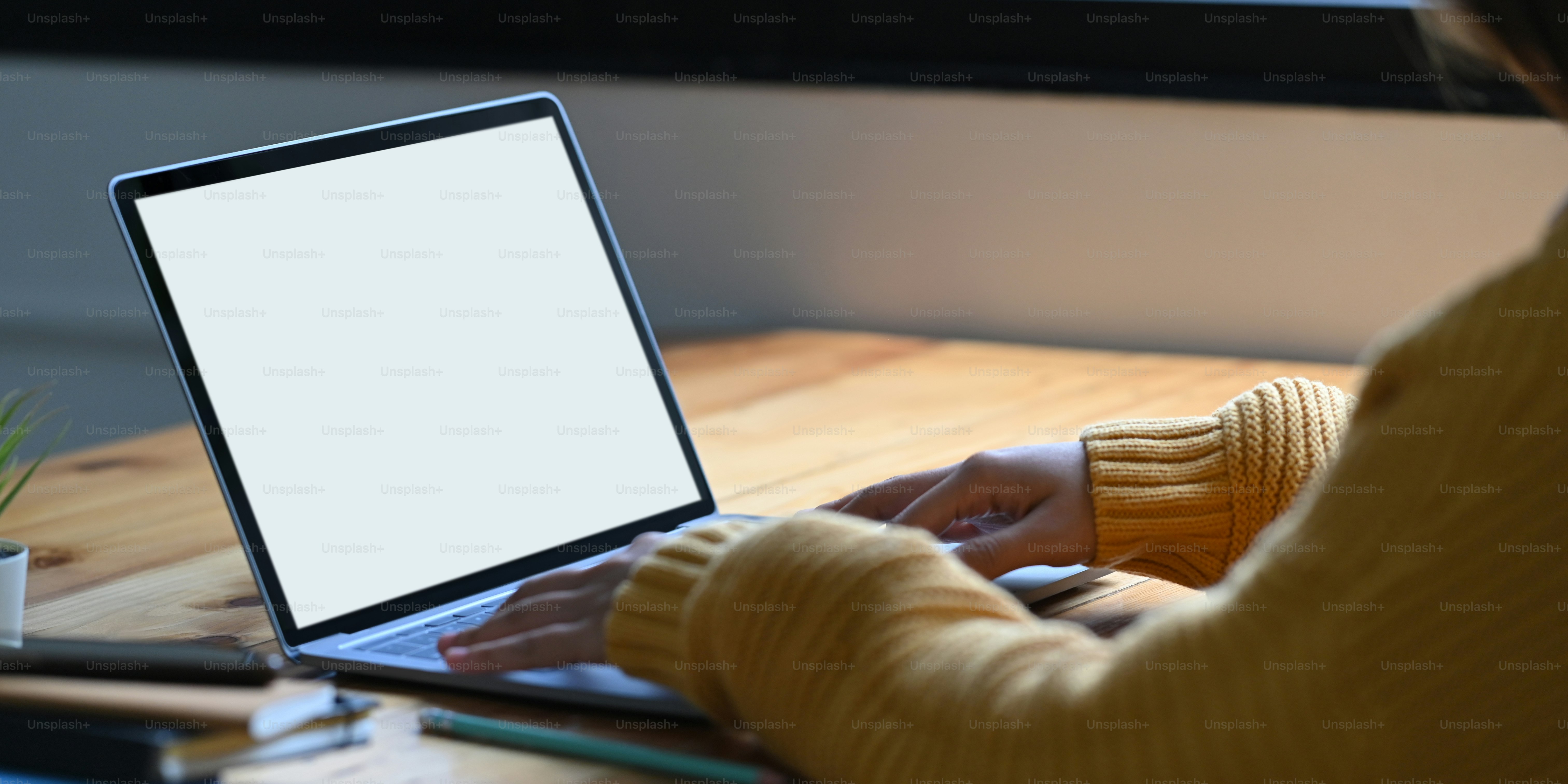 A woman is typing on a white blank screen computer laptop that putting on a wooden working desk.