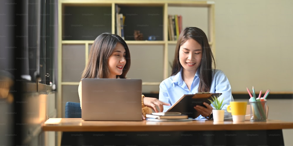 Women are working together with a computer laptop and clipboard at the wooden working desk.