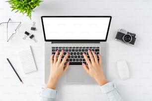 Elegant workspace. Young woman’s hands using laptop with blank display. Top view